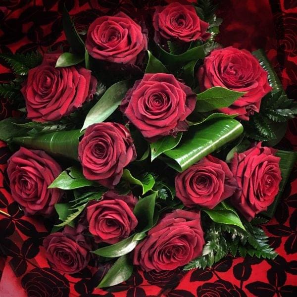 Bob features twelve red roses arranged with green leaves and ferns, set against a striking red and black patterned background.