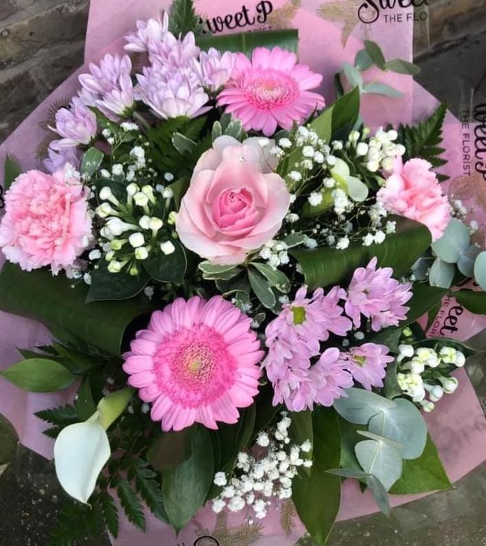 A bouquet featuring pink roses, gerbera daisies, carnations, lilacs, white calla lily, baby's breath, and mixed foliage.