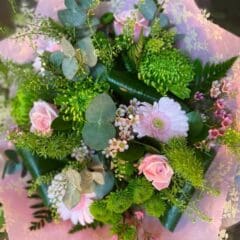 Pastel flower bouquet with pink roses, pink gerbera daisies, green chrysanthemums, eucalyptus leaves, and delicate greenery wrapped in pink floral paper.